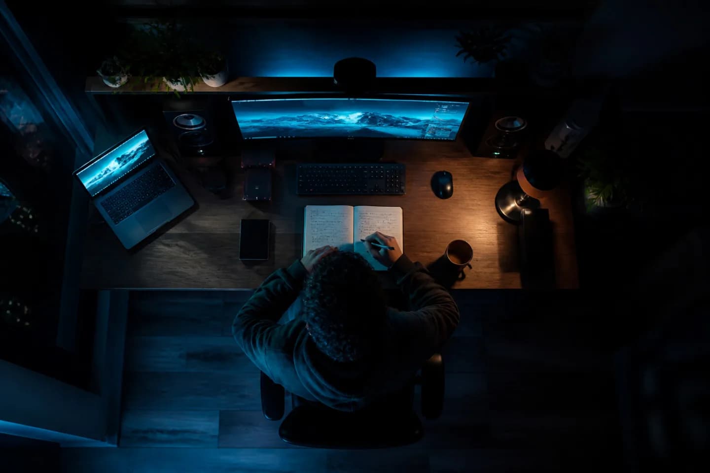 Aerial view of a person writing in a notebook at a glowing desk in a dark room